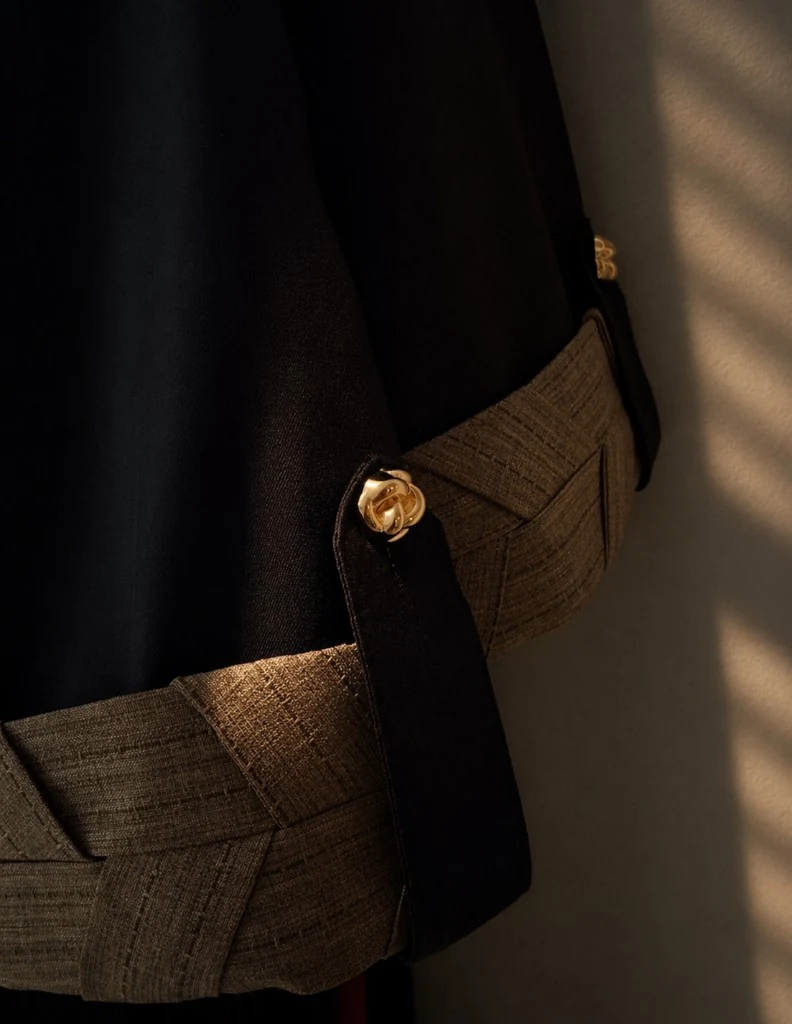 Close-up cuff Knightsbridge Khous Jacket Abaya Bint Saeed dalam Dark Brown — jalur cuff tenunan lebar terinspirasi Khous dengan butang emas Knotted Line signature pada flap lengan. Butiran kraf warisan Al Khous pada outerwear sopan Emirati kontemporari dari Abu Dhabi, Emiriah Arab Bersatu. Dihasilkan di Abu Dhabi. Penghantaran ke seluruh dunia. Bint Saeed Abu Dhabi, Emiriah Arab Bersatu.