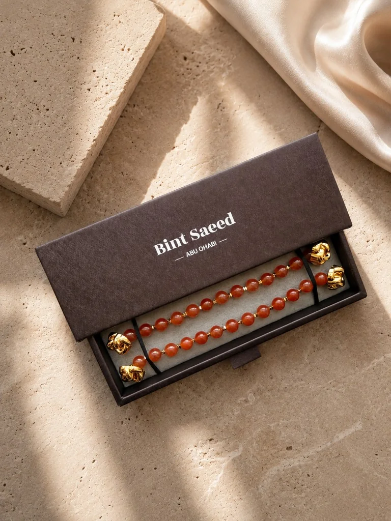 Kotak hadiah Signature Strands carnelian | Perhiasan Marylebone Abaya Bint Saeed Abu Dhabi Presentasi hadiah Signature Strands Bint Saeed untuk Marylebone Abaya — strand batu carnelian alam tembus dengan ujung Knotted Line emas dalam kotak bermerek Bint Saeed Abu Dhabi di atas batu dengan sutra. Perhiasan batu alam lepas untuk abaya desainer. Abaya desainer mewah dengan perhiasan batu alam Bint Saeed Abu Dhabi, UEA — abaya A-line anggun dengan Onyx Strands lepas dan Signature Strands dapat dipertukarkan untuk penggemar fashion, editor fashion, kurator, audiens warisan budaya, diplomat, pembukaan galeri, dan lemari internasional di London, Paris, Riyadh, Doha, dan dunia. Dibuat di Abu Dhabi. Pengiriman dunia. Bint Saeed Abu Dhabi, Uni Emirat Arab.