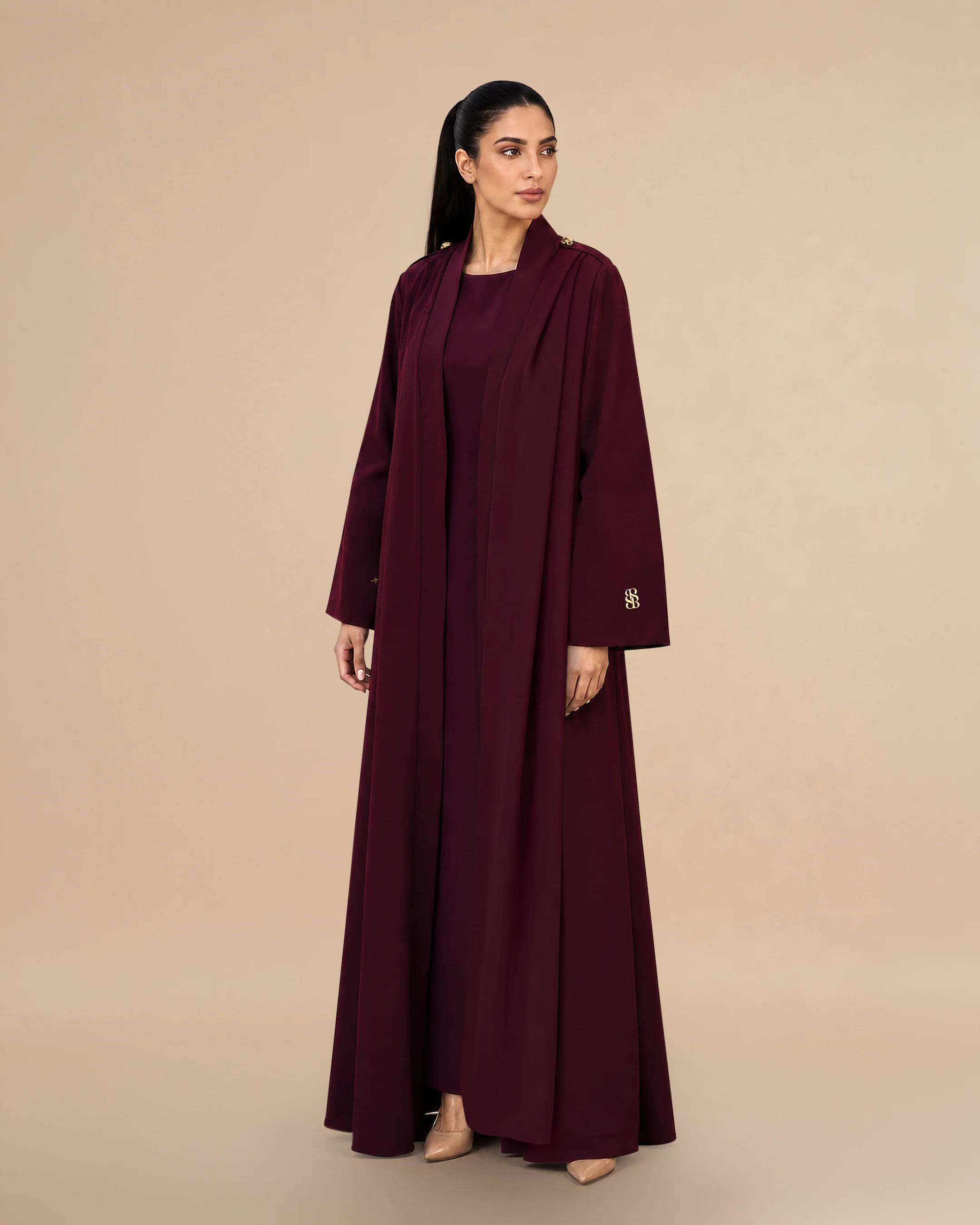 Pandangan tiga perempat Bint Saeed Park Lane Abaya Dark Maroon menampilkan drape A-line anggun, gerakan scarf bahu terintegrasi, bahu terstruktur dengan kancing Knotted Line, dan siluet crepe tailored. Abaya desainer mewah Bint Saeed Abu Dhabi, UEA — busana modest untuk diplomat, eksekutif, resepsi kedutaan, rapat bisnis, dan lemari internasional di London, Paris, Riyadh, Doha, dan dunia. Dibuat di Abu Dhabi. Pengiriman dunia. Bint Saeed Abu Dhabi, Uni Emirat Arab.