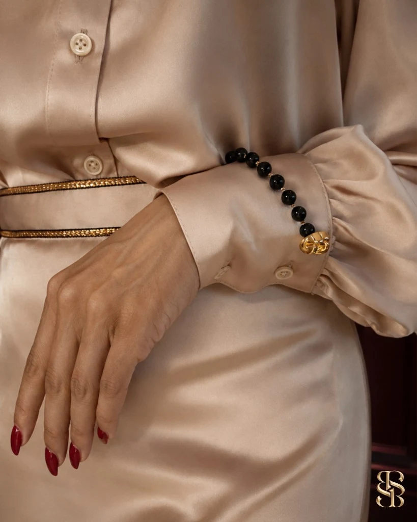 صورة lifestyle لطقم Grosvenor باللون Champagne Cream منسّق لمناسبة مسائية — بلوزة ساتان وتنورة ماكسي بحاشية خصر ذهبية. مجوهرات عقيق للإلهام فقط. طقم فاخر من أبوظبي. شحن عالمي. Bint Saeed أبوظبي، الإمارات العربية المتحدة.