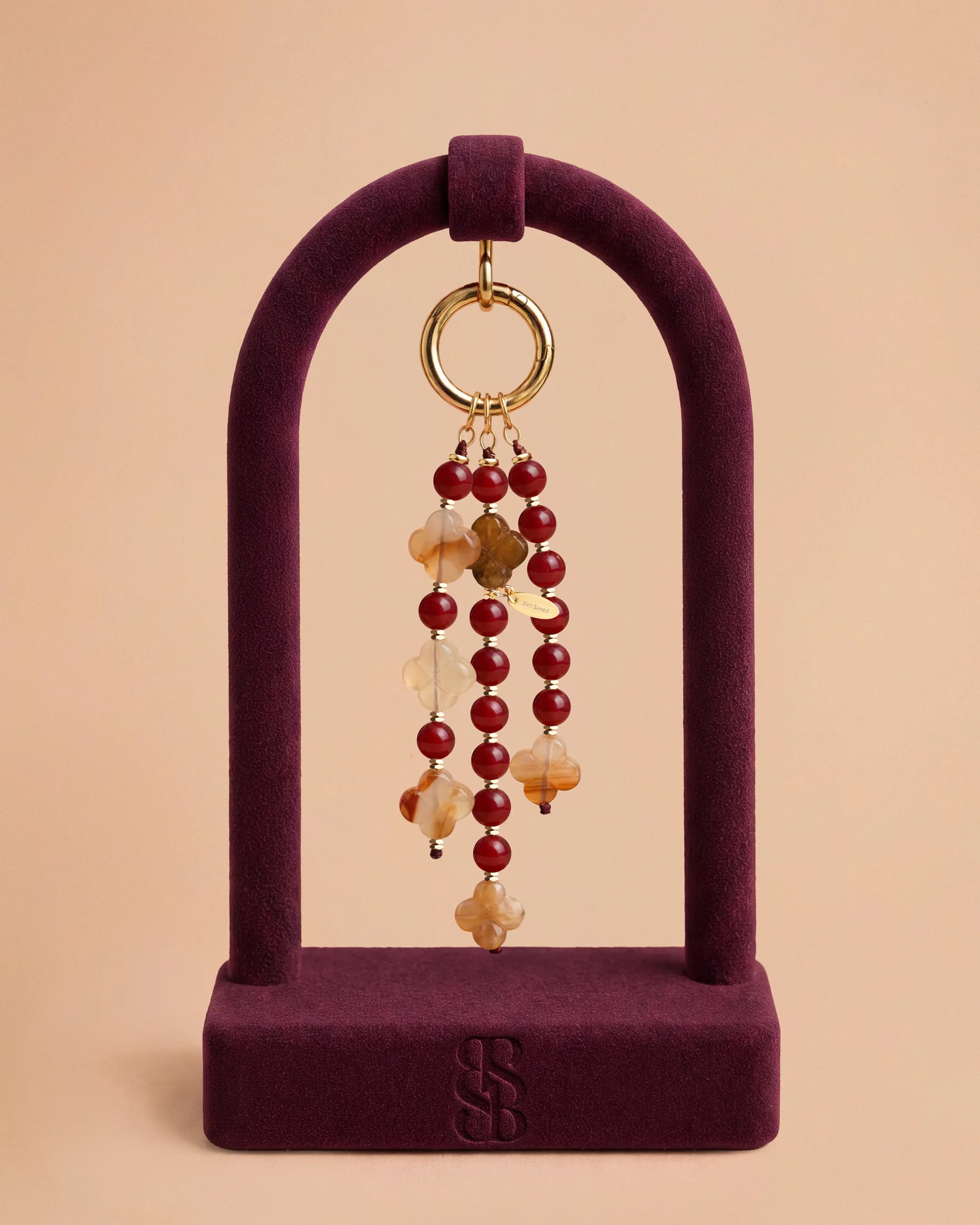 Liontin tas Al Ain Oasis II jade fuchsia — tiga untaian menjuntai jade fuchsia dengan Rosette Al Ain ukiran tangan, aksesori tas mewah batu alam Bint Saeed Abu Dhabi. Bint Saeed Abu Dhabi, Uni Emirat Arab.