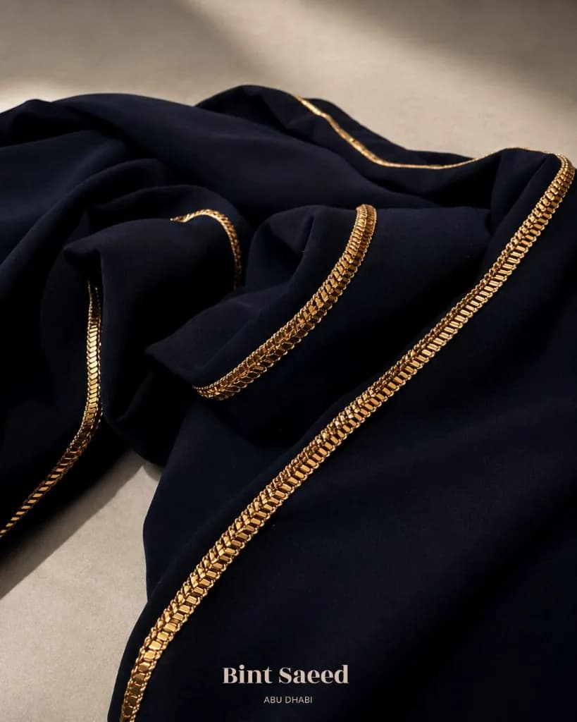 Al Talli gold trim on deep abaya fabric, Emirati heritage craft, Bint Saeed Abu Dhabi. Bint Saeed Abu Dhabi, United Arab Emirates.