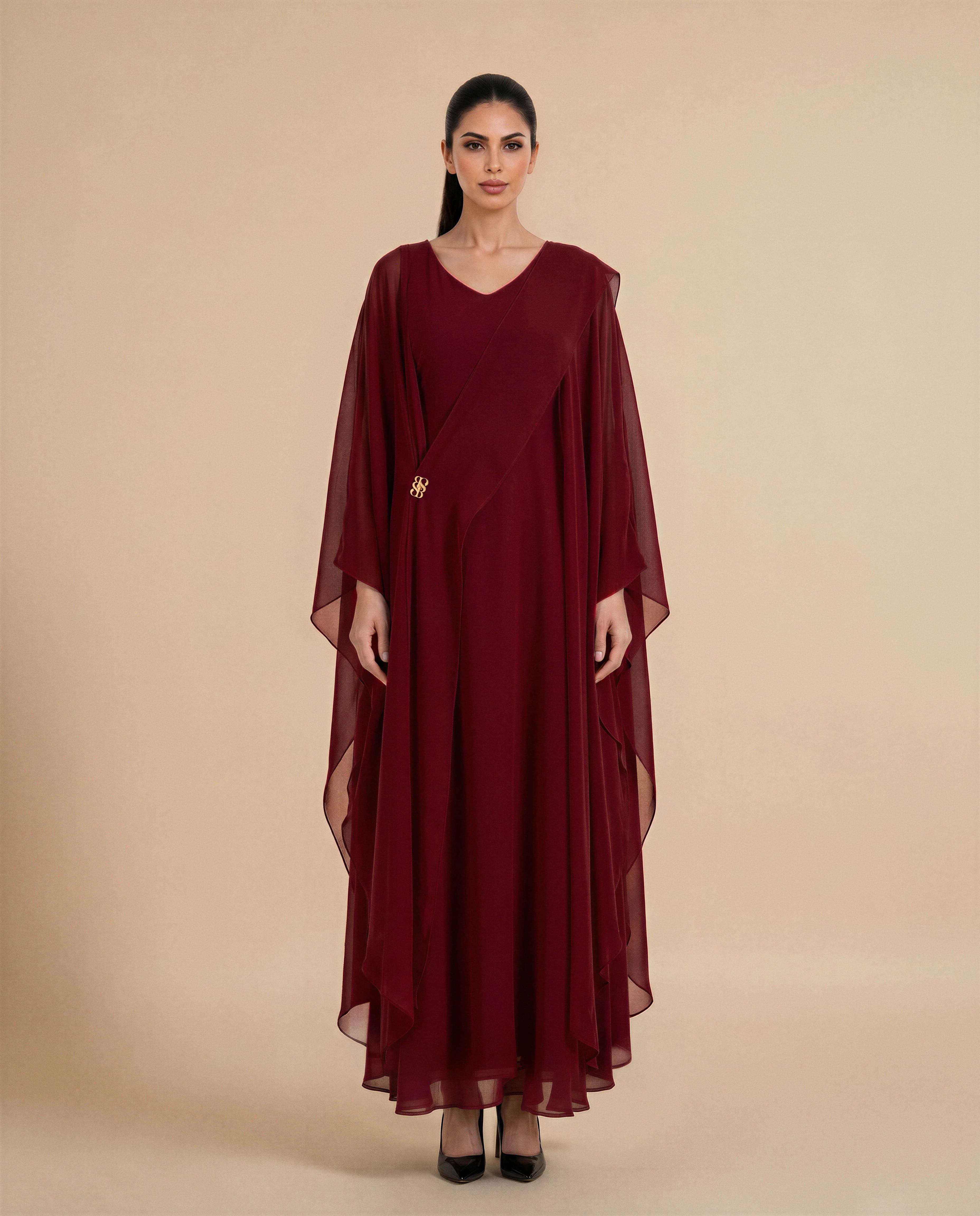 Kaftan Mayfair dalam kain chiffon crepe Merah Marun Gelap, tampak depan. Kaftan mewah wanita untuk acara dari Bint Saeed Abu Dhabi, Uni Emirat Arab, menampilkan garis leher V, siluet mengalir, detail syal melekat, dan lambang emas khas.