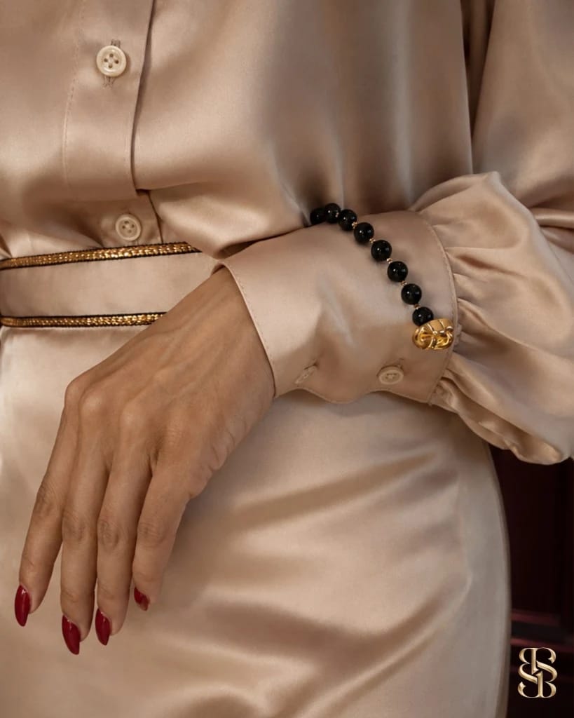 صورة lifestyle لطقم Grosvenor باللون Champagne Cream منسّق لمناسبة مسائية — بلوزة ساتان وتنورة ماكسي بحاشية خصر ذهبية. مجوهرات عقيق للإلهام فقط. طقم فاخر من أبوظبي. شحن عالمي. Bint Saeed أبوظبي، الإمارات العربية المتحدة.