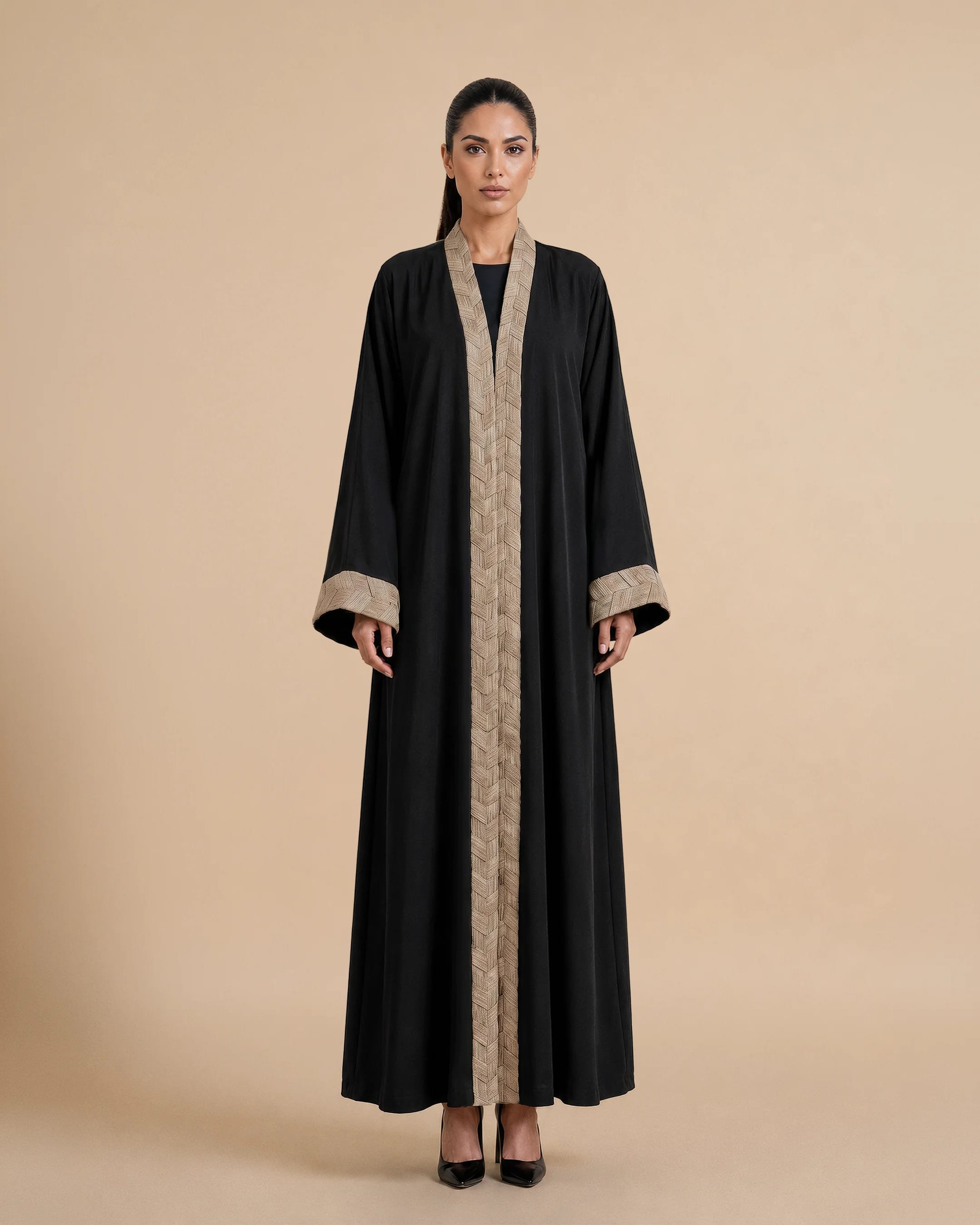 Abaya Belgravia dalam Hitam Pekat, tampak depan. Abaya mewah terinspirasi Bisht dari Bint Saeed Abu Dhabi, Uni Emirat Arab, menampilkan trim tenun tangan terinspirasi tradisi anyaman Khous Emirati dan siluet depan terbuka yang elegan.