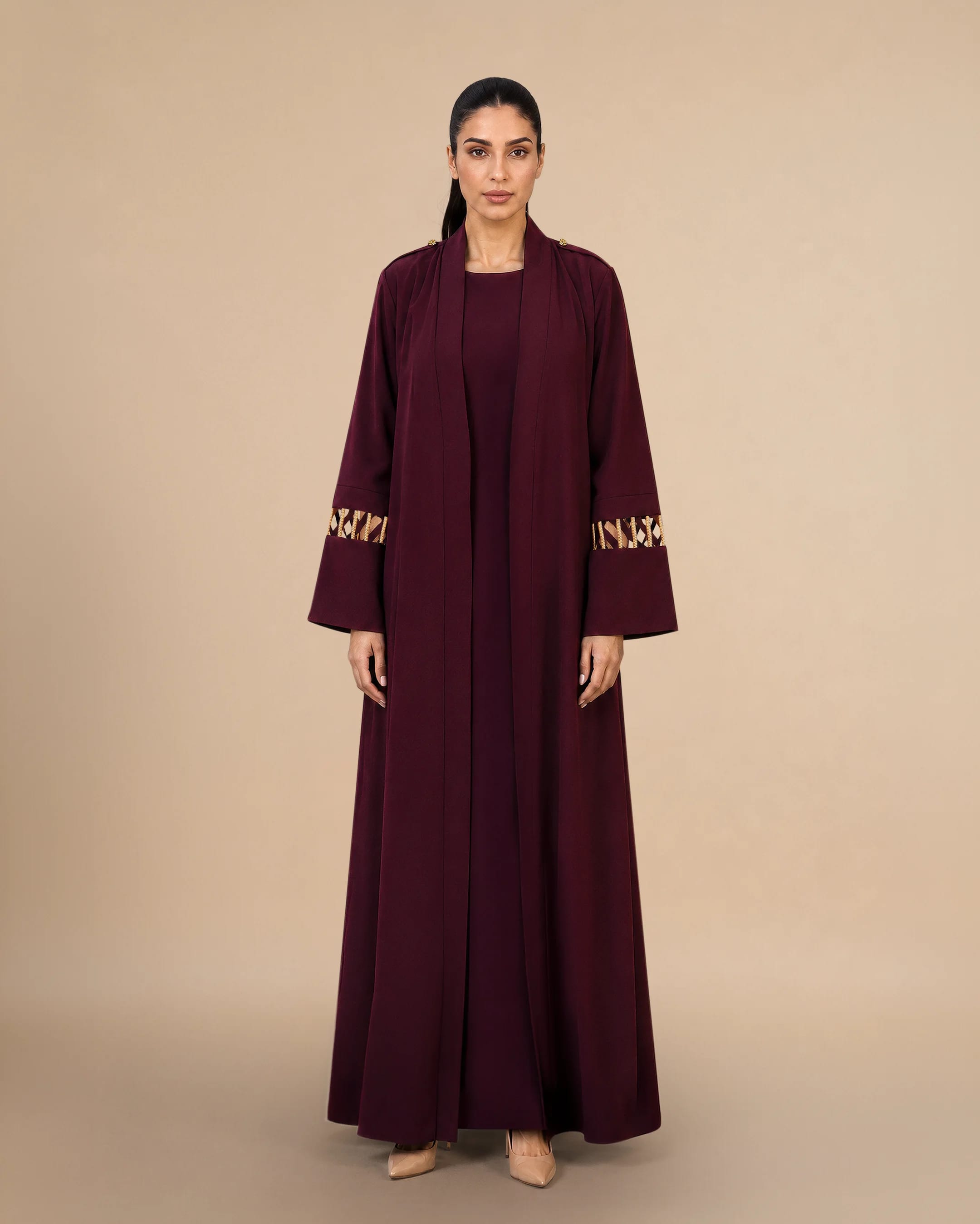 Bint Saeed Covent Garden Al Talli Abaya Burgundy, tampak depan. Abaya desainer mewah A-line dengan trim Al Talli tenun tradisional Emirati yang diakui UNESCO, epaulet Knotted Line emas signature, dan siluet depan terbuka elegan. Beli abaya Al Talli UEA — busana modest warisan dan kerajinan Emirati kontemporer dari Dubai dan Abu Dhabi ke GCC dan dunia. Dibuat di Abu Dhabi, UEA. Pengiriman dunia. Bint Saeed Abu Dhabi, Uni Emirat Arab.