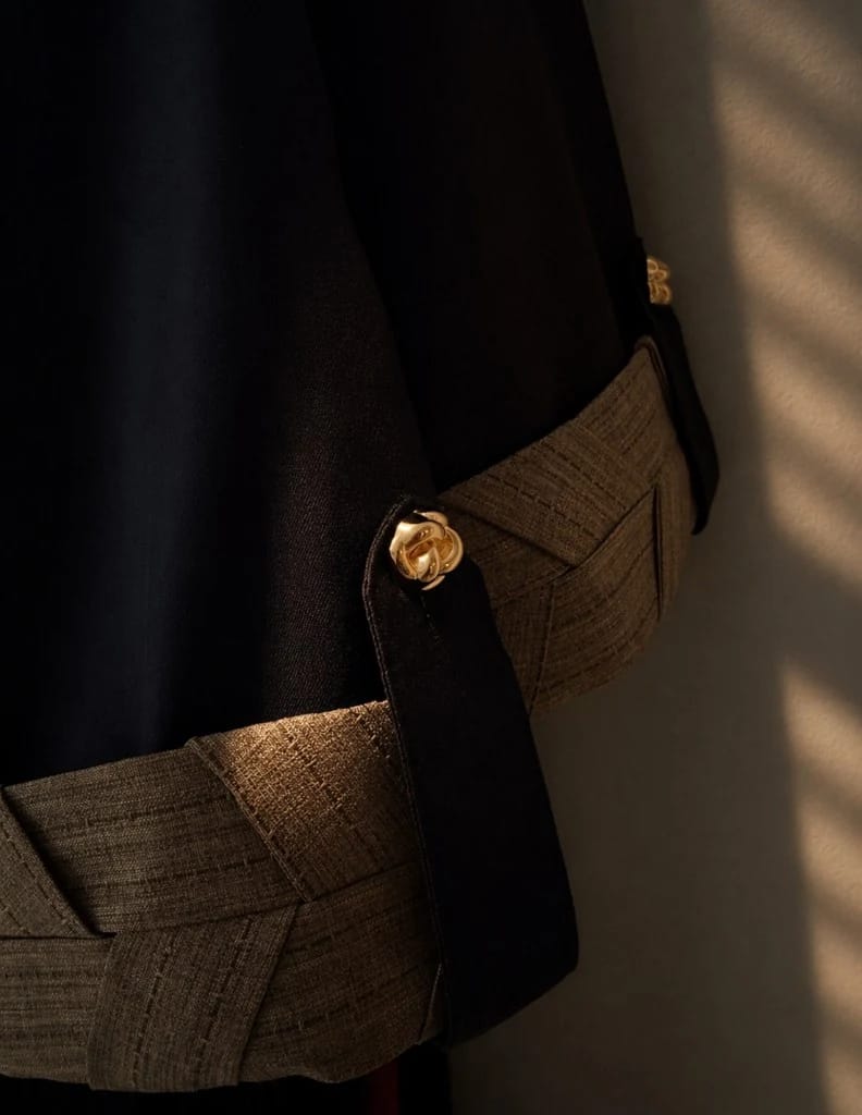 Knightsbridge Abaya Jacket Dark Brown — close-up manset | Khous | Bint Saeed Abu Dhabi Close-up manset Knightsbridge Khous Jacket Abaya Bint Saeed dalam Dark Brown — pita manset tenun lebar terinspirasi Khous dengan kancing emas Knotted Line signature pada flap lengan. Detail kerajinan warisan Al Khous pada outerwear modest Emirati kontemporer dari Abu Dhabi, Uni Emirat Arab. Dibuat di Abu Dhabi. Pengiriman ke seluruh dunia. Bint Saeed Abu Dhabi, Uni Emirat Arab.