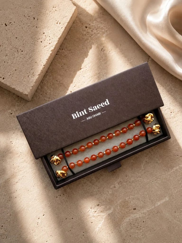 Kotak hadiah Signature Strands carnelian | Perhiasan Marylebone Abaya Bint Saeed Abu Dhabi Presentasi hadiah Signature Strands Bint Saeed untuk Marylebone Abaya — strand batu carnelian alam tembus dengan ujung Knotted Line emas dalam kotak bermerek Bint Saeed Abu Dhabi di atas batu dengan sutra. Perhiasan batu alam lepas untuk abaya desainer. Abaya desainer mewah dengan perhiasan batu alam Bint Saeed Abu Dhabi, UEA — abaya A-line anggun dengan Onyx Strands lepas dan Signature Strands dapat dipertukarkan untuk penggemar fashion, editor fashion, kurator, audiens warisan budaya, diplomat, pembukaan galeri, dan lemari internasional di London, Paris, Riyadh, Doha, dan dunia. Dibuat di Abu Dhabi. Pengiriman dunia. Bint Saeed Abu Dhabi, Uni Emirat Arab.