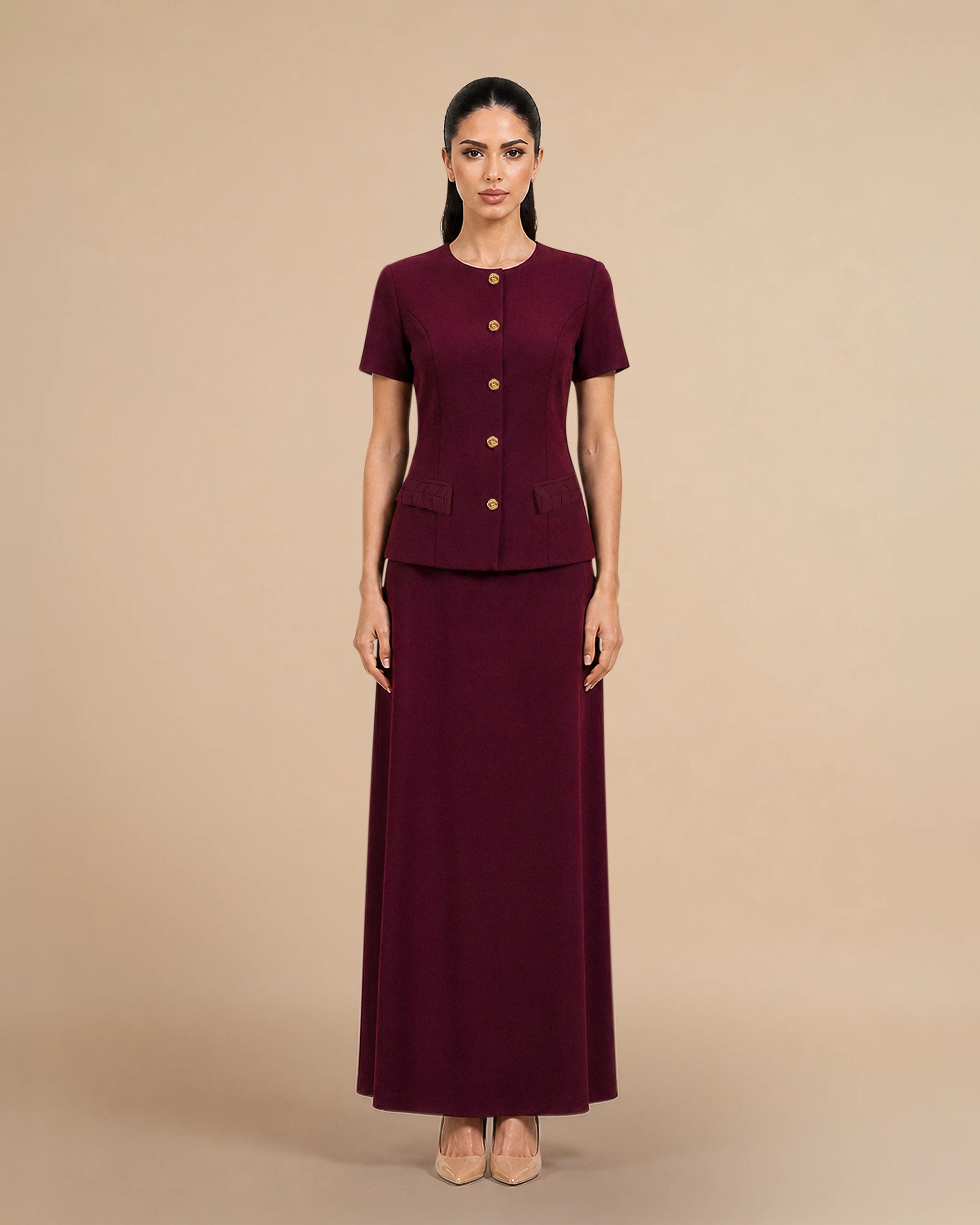 Covent Garden Signature Set in Burgundy, tampak depan. Contemporary dua potong dress and short-sleeve terstruktur jacket oleh Bint Saeed Abu Dhabi, Uni Emirat Arab, menampilkan Al Khous-inspired woven pocket flaps and signature gold-tone Knotted Line buttons.