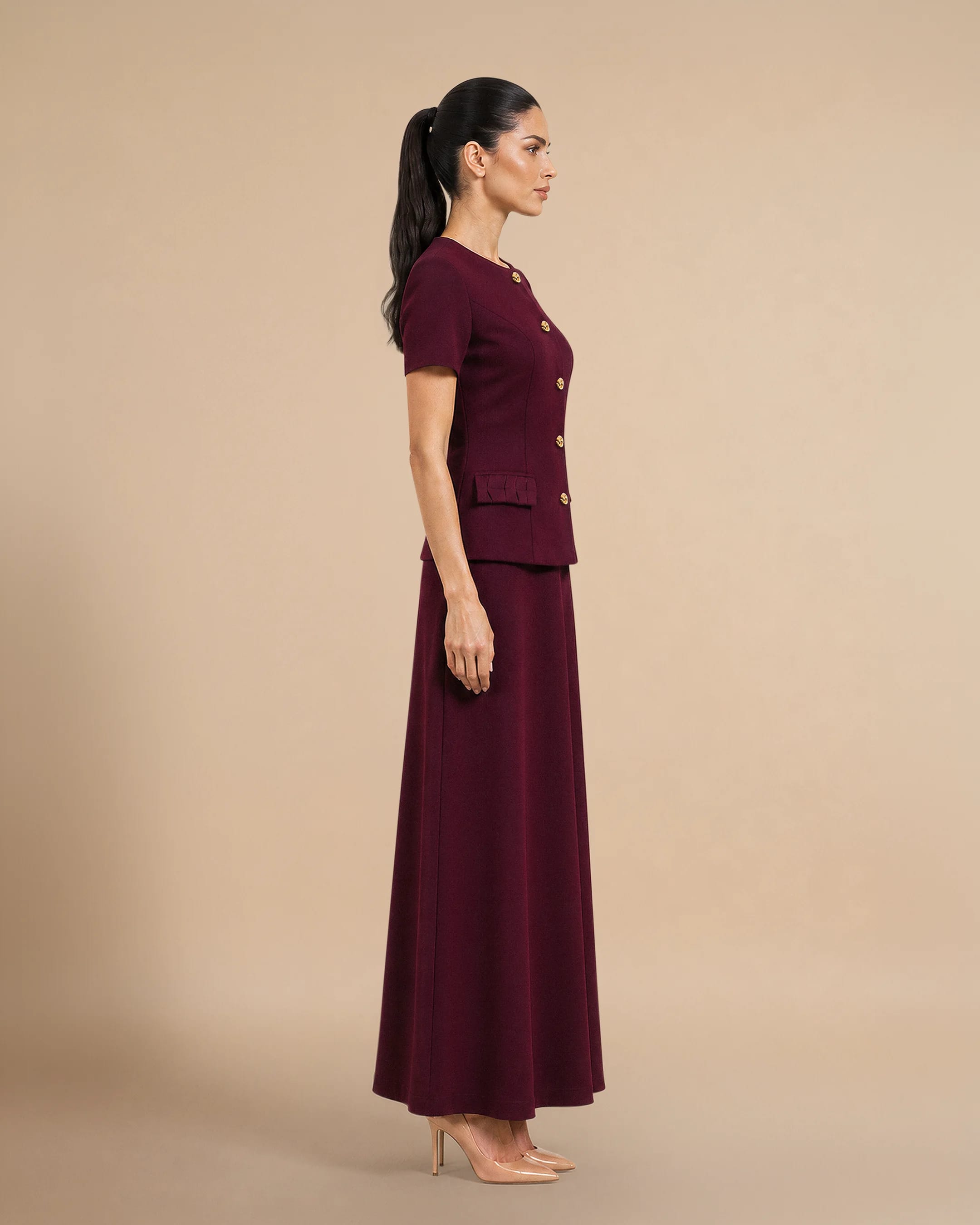 tampak samping of the Covent Garden Signature Set in Burgundy menampilkan the fitted gaun maxi, terstruktur short-sleeve jacket, and refined contemporary silhouette. Premium coordinate set oleh Bint Saeed Abu Dhabi celebrating Emirati heritage through modern womenswear. Bint Saeed Abu Dhabi, Uni Emirat Arab.