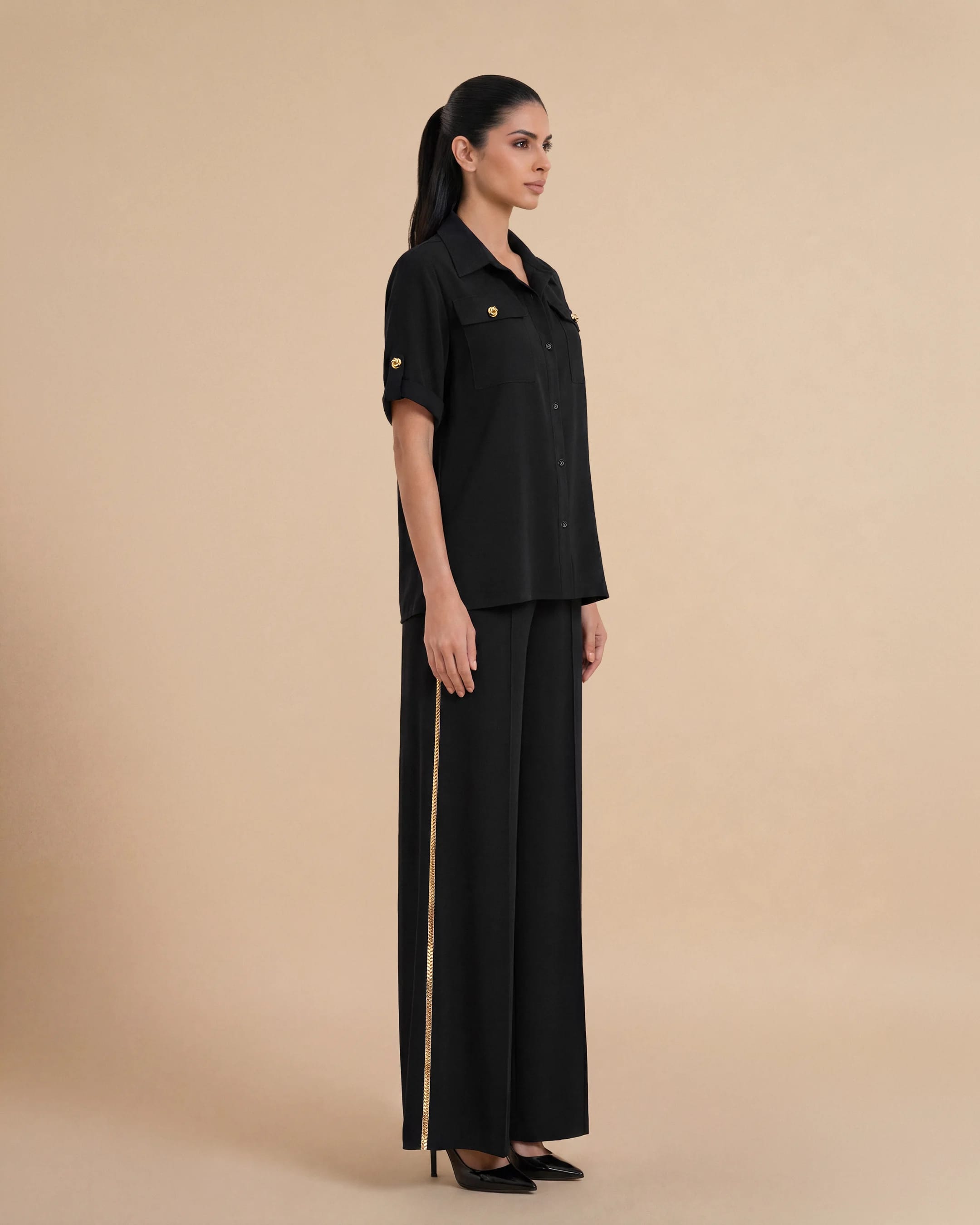 Pandangan tiga perempat Bint Saeed Soho Set Hitam pekat menampilkan drape krepe premium mengalir, siluet kemeja oversized, gerakan palazzo kaki lebar, dan trim Al Talli warisan UNESCO halus di sisi celana. Set perjalanan koordinat Emirati mewah — celana terlaris dan kemeja oversized untuk wanita di Abu Dhabi, Dubai, Doha, GCC, London, Paris, dan garderobe internasional. Dibuat di Abu Dhabi, UEA. Pengiriman dunia. Bint Saeed Abu Dhabi, Uni Emirat Arab.