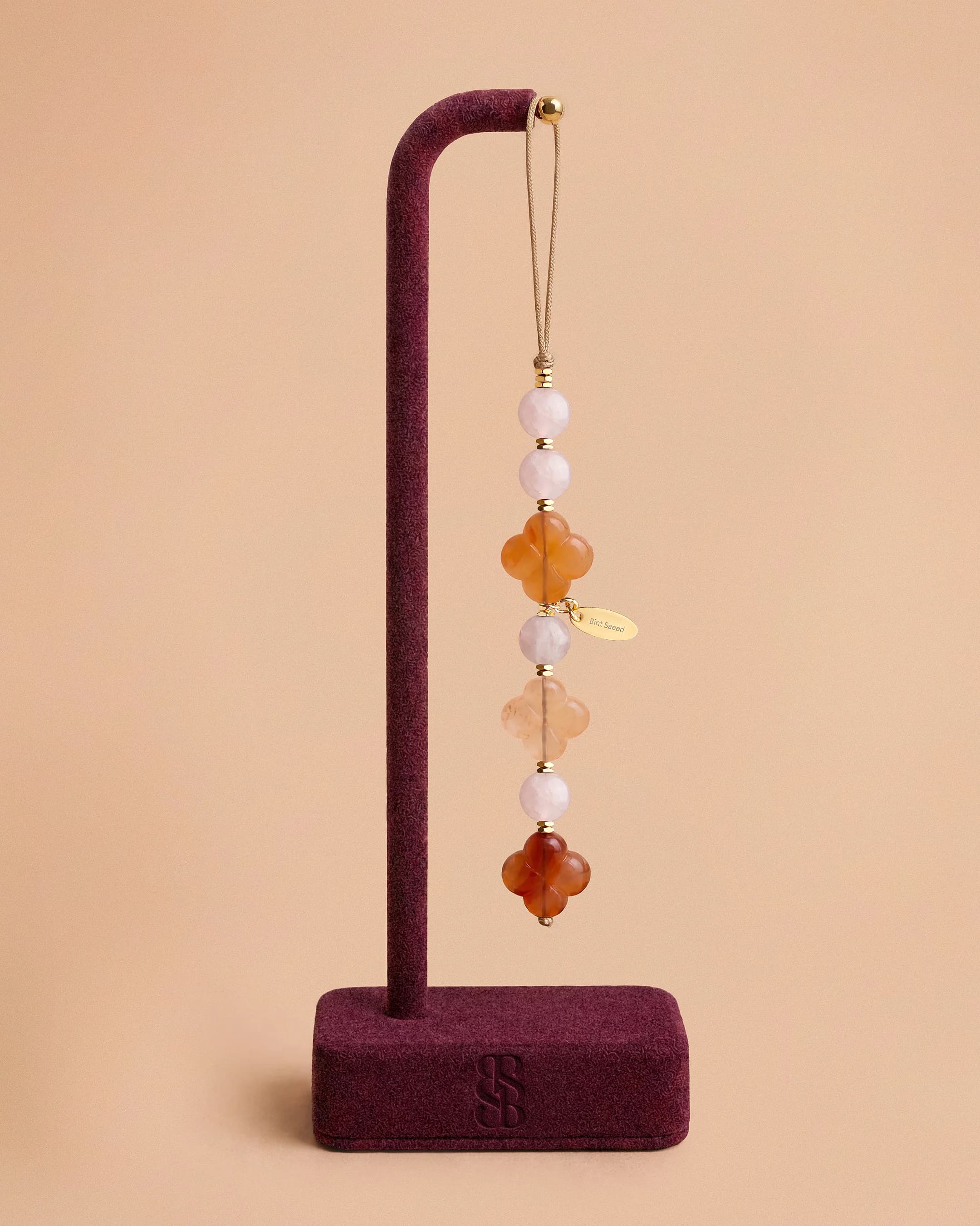 Colgante móvil Al Quaa cuarzo rosa — cuentas de cuarzo rosa blush suave y Roseta de Al Ain en cornalina, accesorio móvil lujo piedra natural Bint Saeed Abu Dabi. Bint Saeed Abu Dabi, Emiratos Árabes Unidos.