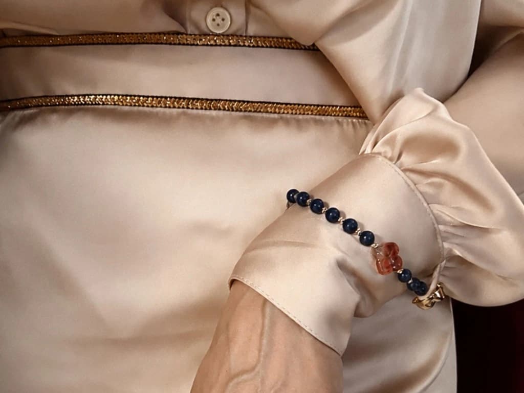 Bint Saeed Signature Strand with lapis lazuli beads and Al Ain Rosette carnelian, attached to the cuff of a champagne silk blouse. Bint Saeed Abu Dhabi, United Arab Emirates.