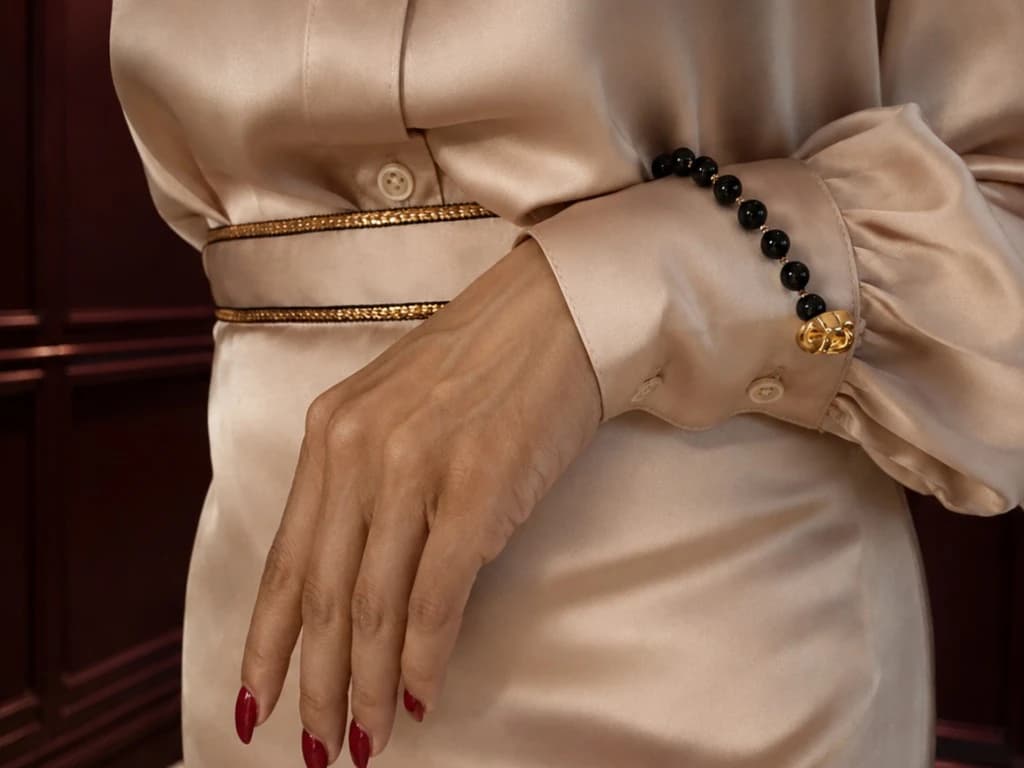 Bint Saeed Signature Strand with onyx beads and gold-tone clasp, attached to the cuff of a champagne silk blouse. Bint Saeed Abu Dhabi, United Arab Emirates.