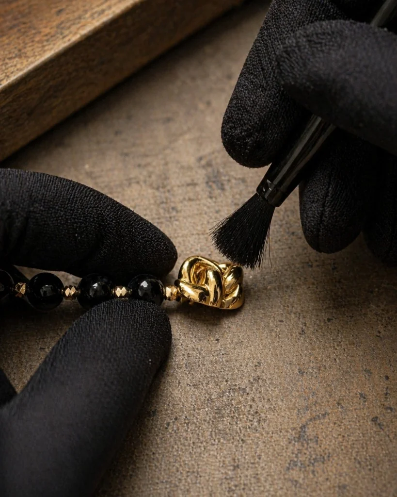 Atelier finishing of a gold knot charm on a black beaded strand with gloved hands. Bint Saeed Abu Dhabi, United Arab Emirates.