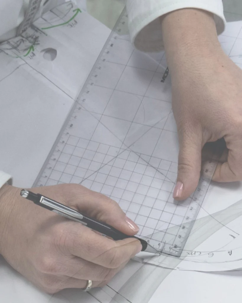 Hands drafting an abaya pattern with pencil and ruler during Phase I development. Bint Saeed Abu Dhabi, United Arab Emirates.